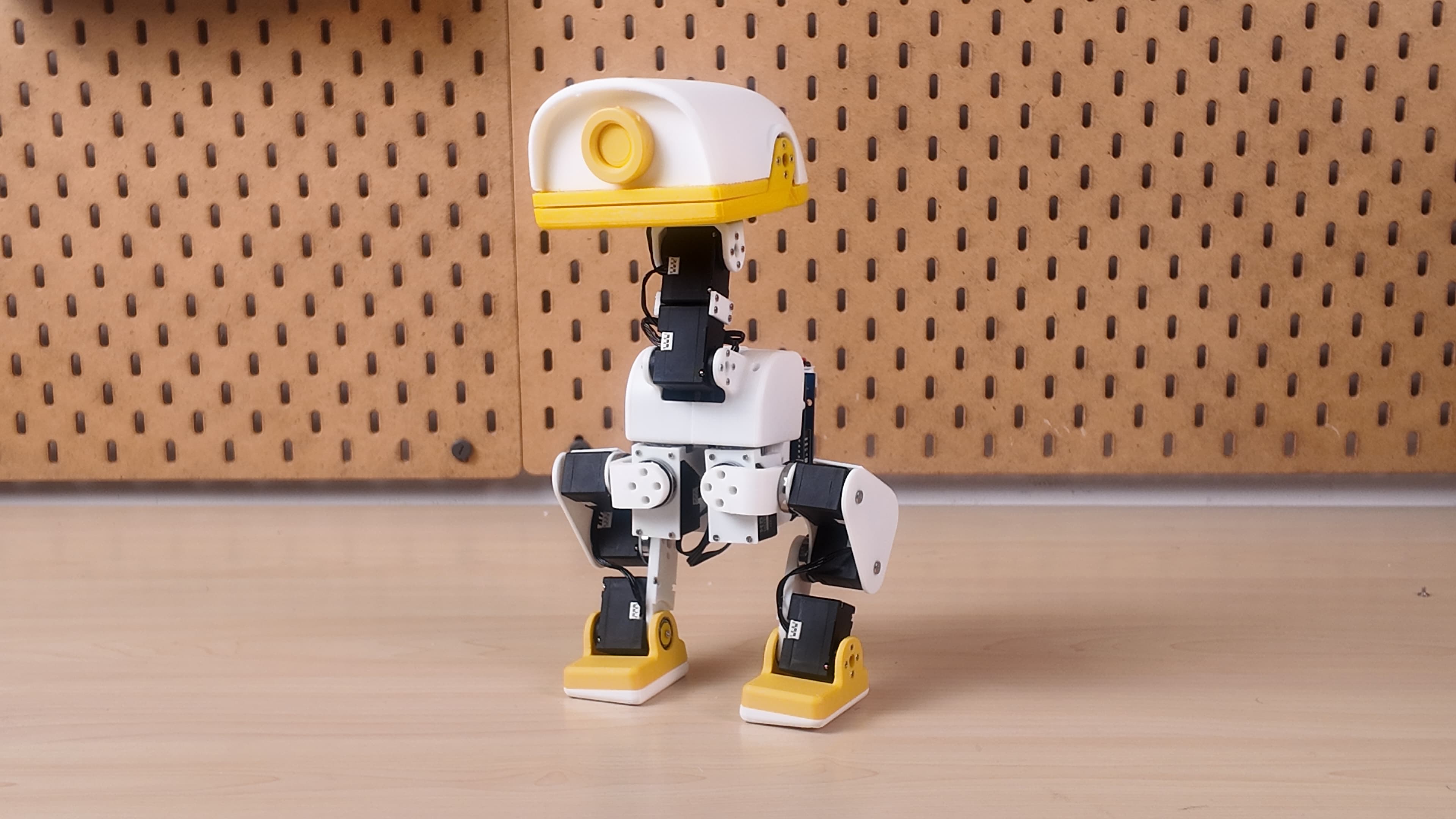 XGO-Duck standing on a workbench, with a white body, yellow beak and feet, and articulated legs.