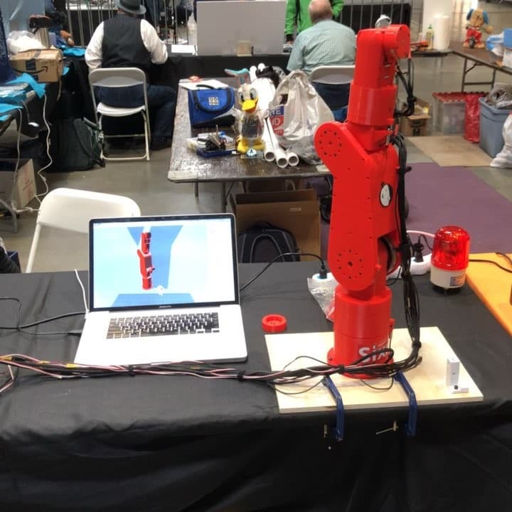 Red robot arm displayed on a table beside a laptop.