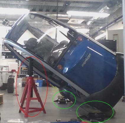 A blue hard-canopy scooter vehicle tilted on axle stands in a workshop.