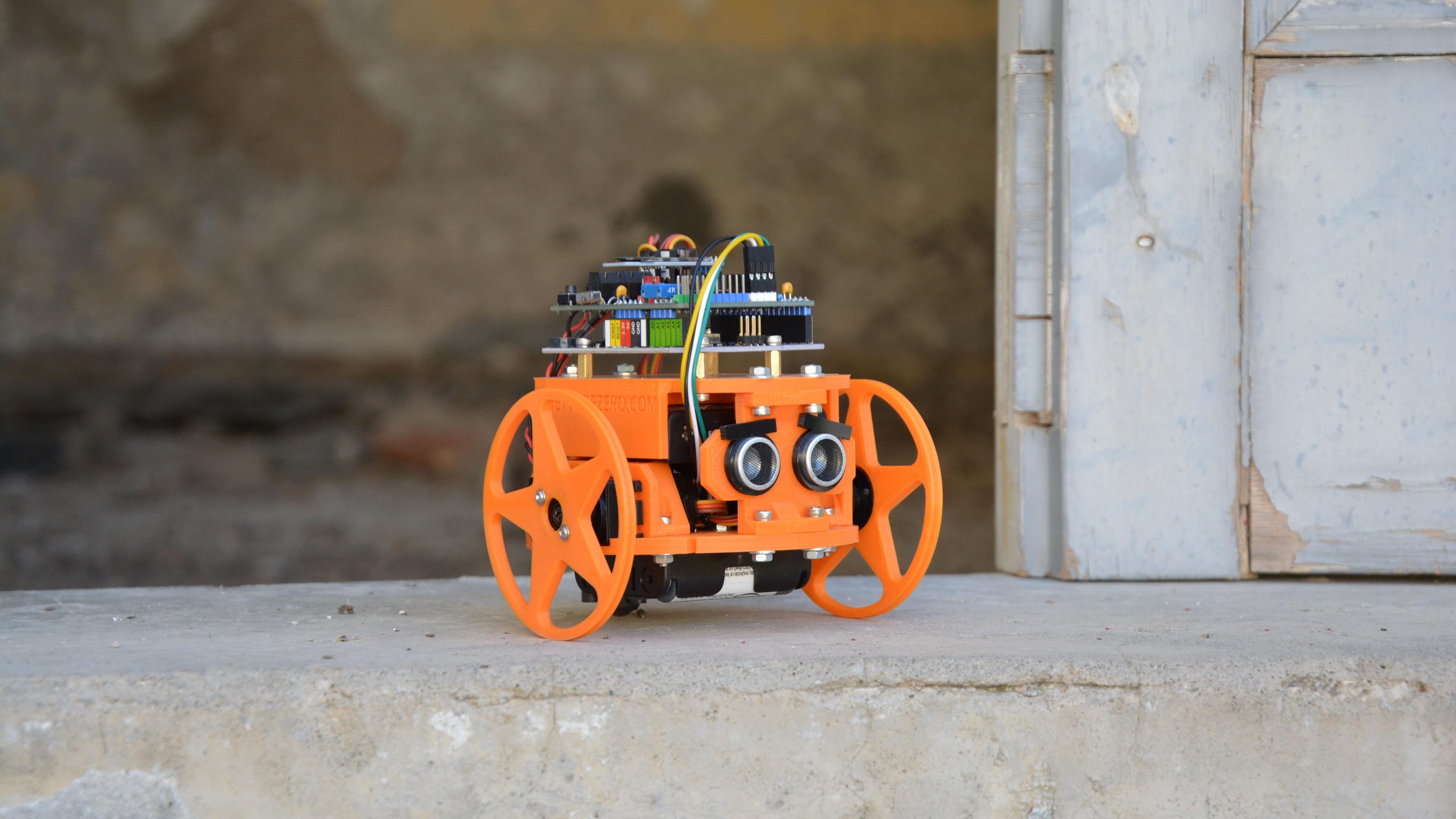 An orange wheeled robot with an Arduino board mounted on top.