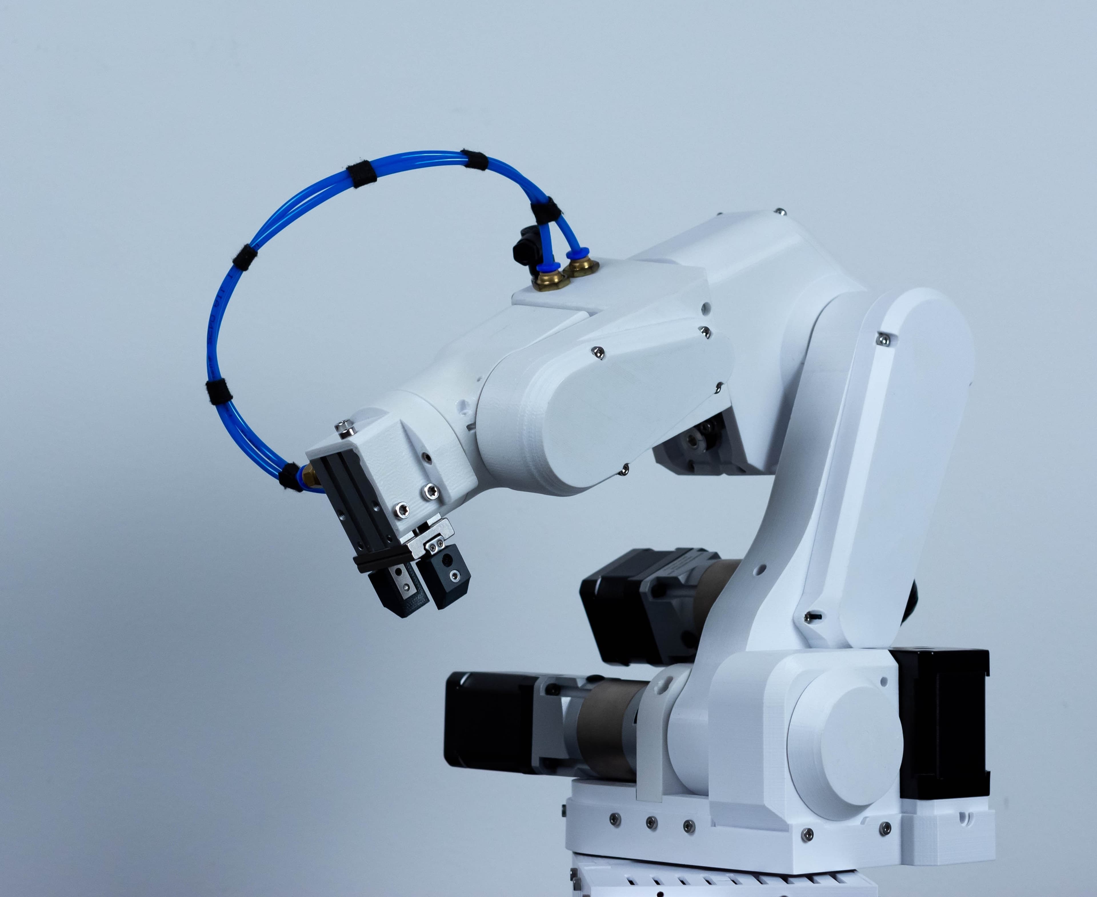 White desktop robotic arm with a gripper and blue tubing against a pale blue background.