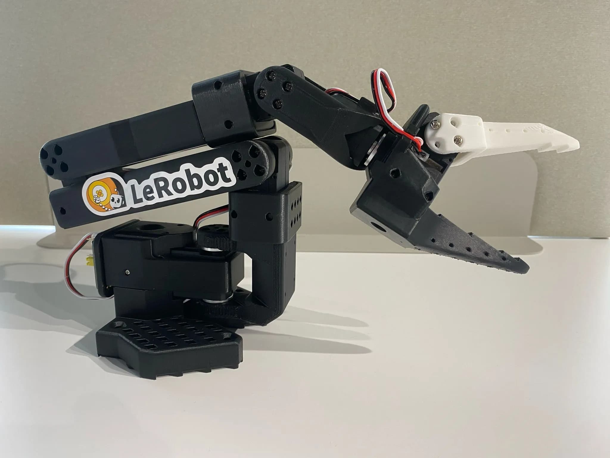 SO-101 follower arm: black 3D-printed links, a white gripper jaw and a LeRobot sticker