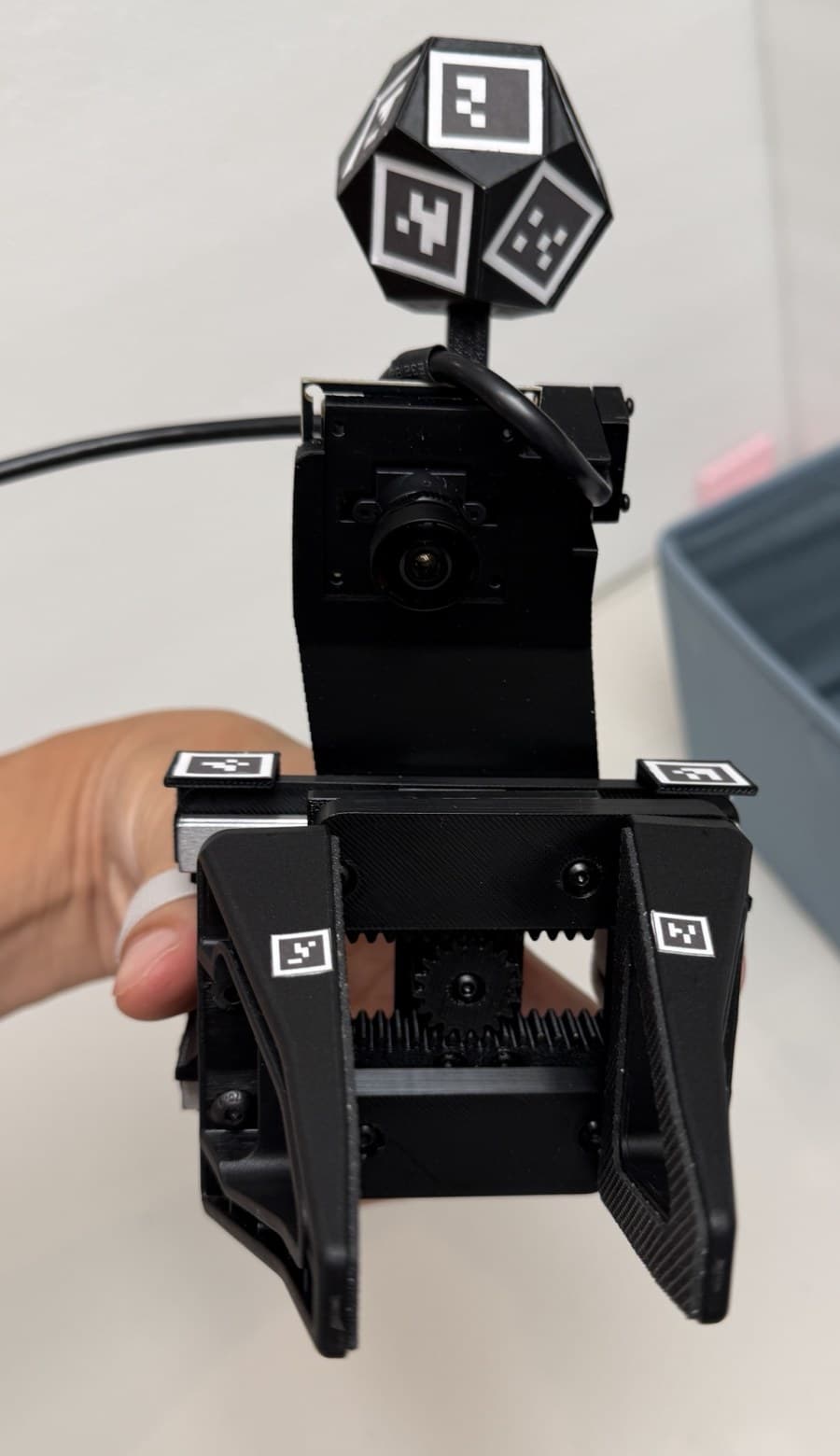 The YAM-UMI gripper worn on a hand, with its fingers, markers, wrist camera and marker ball visible.