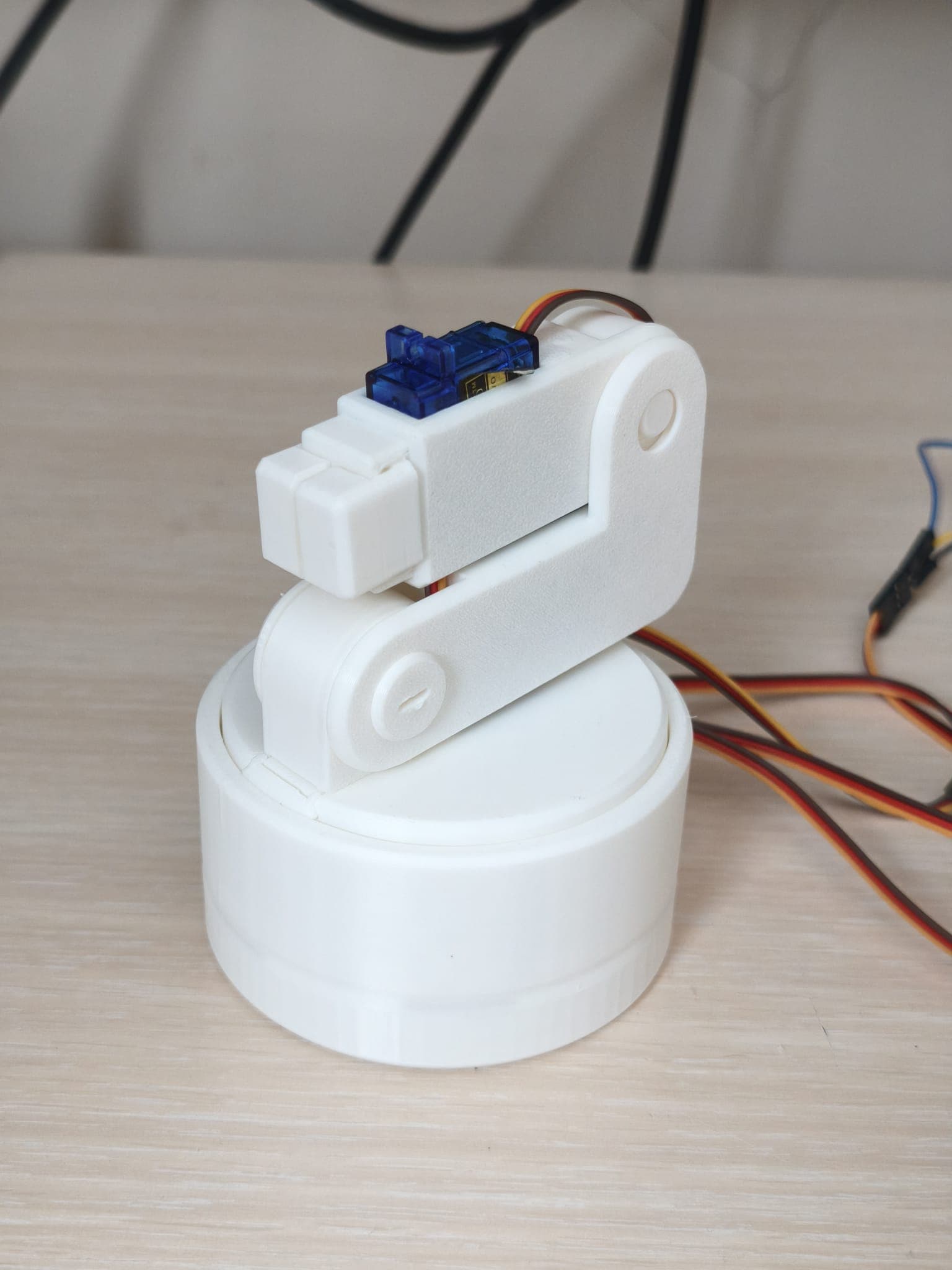 White desktop robot arm with blue servos, photographed on a table.