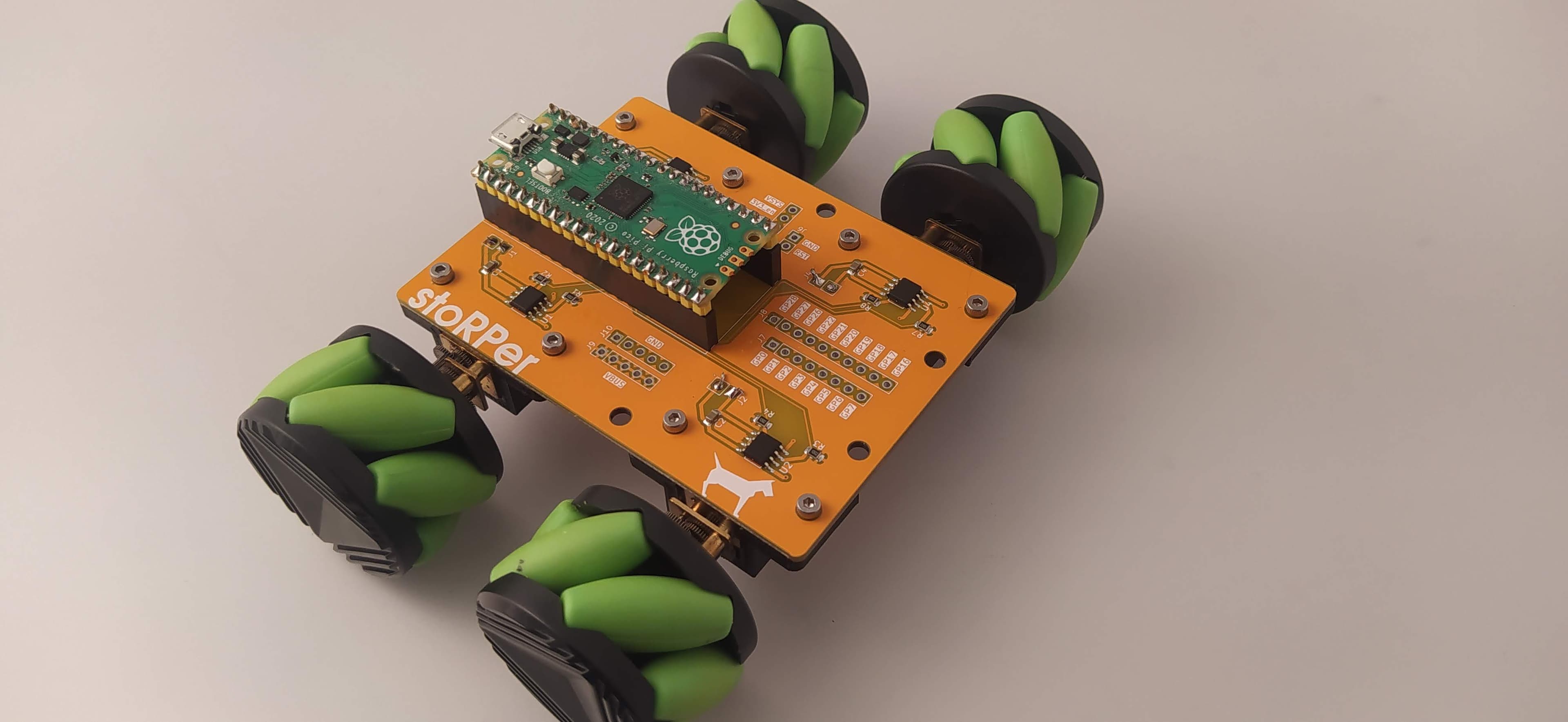 An orange rover PCB with a controller board and four black-and-green wheels.