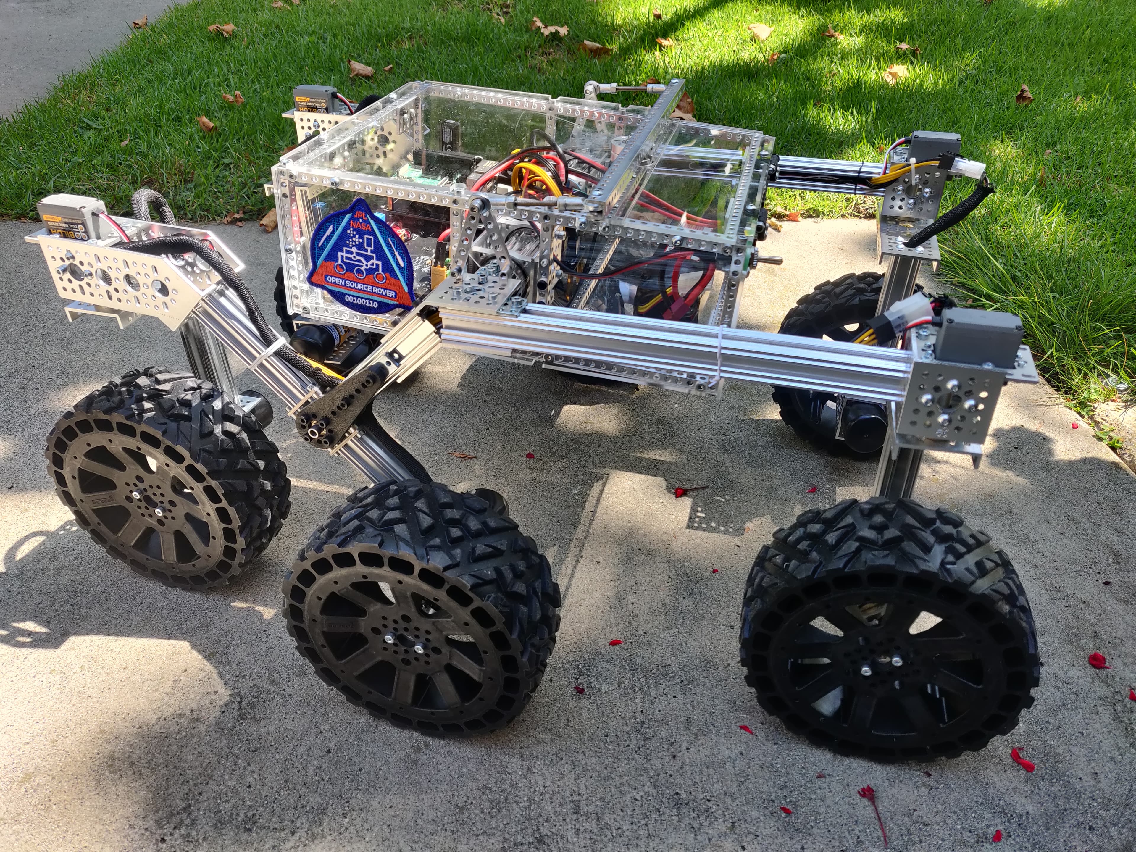 The Open Source Rover on a sidewalk: aluminium frame, clear electronics box and six large off-road wheels