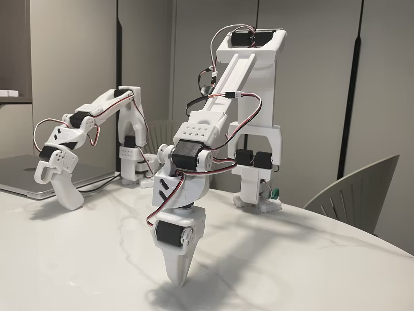 A white robotic arm with a gripper shown on a table.