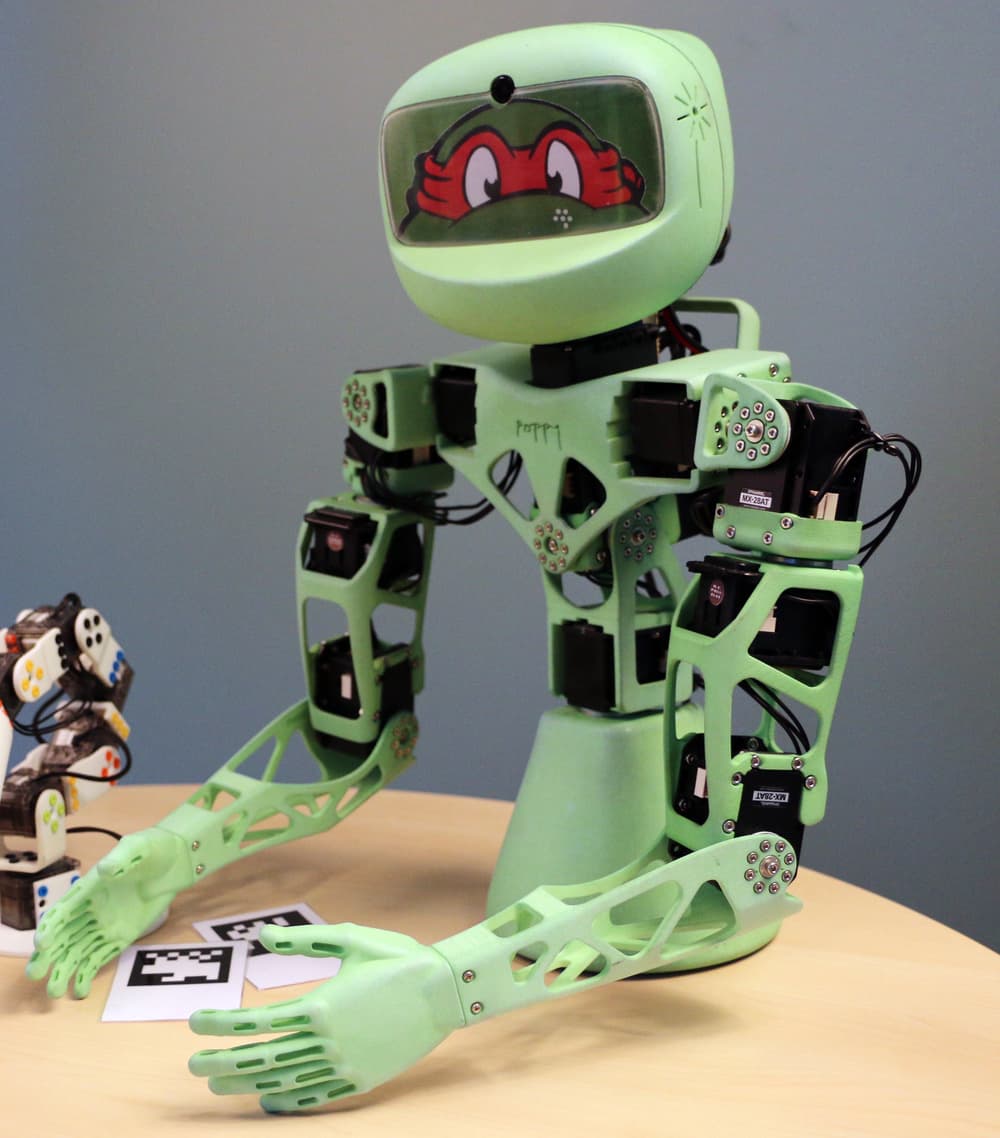 A green Poppy Torso robot mounted on a table.