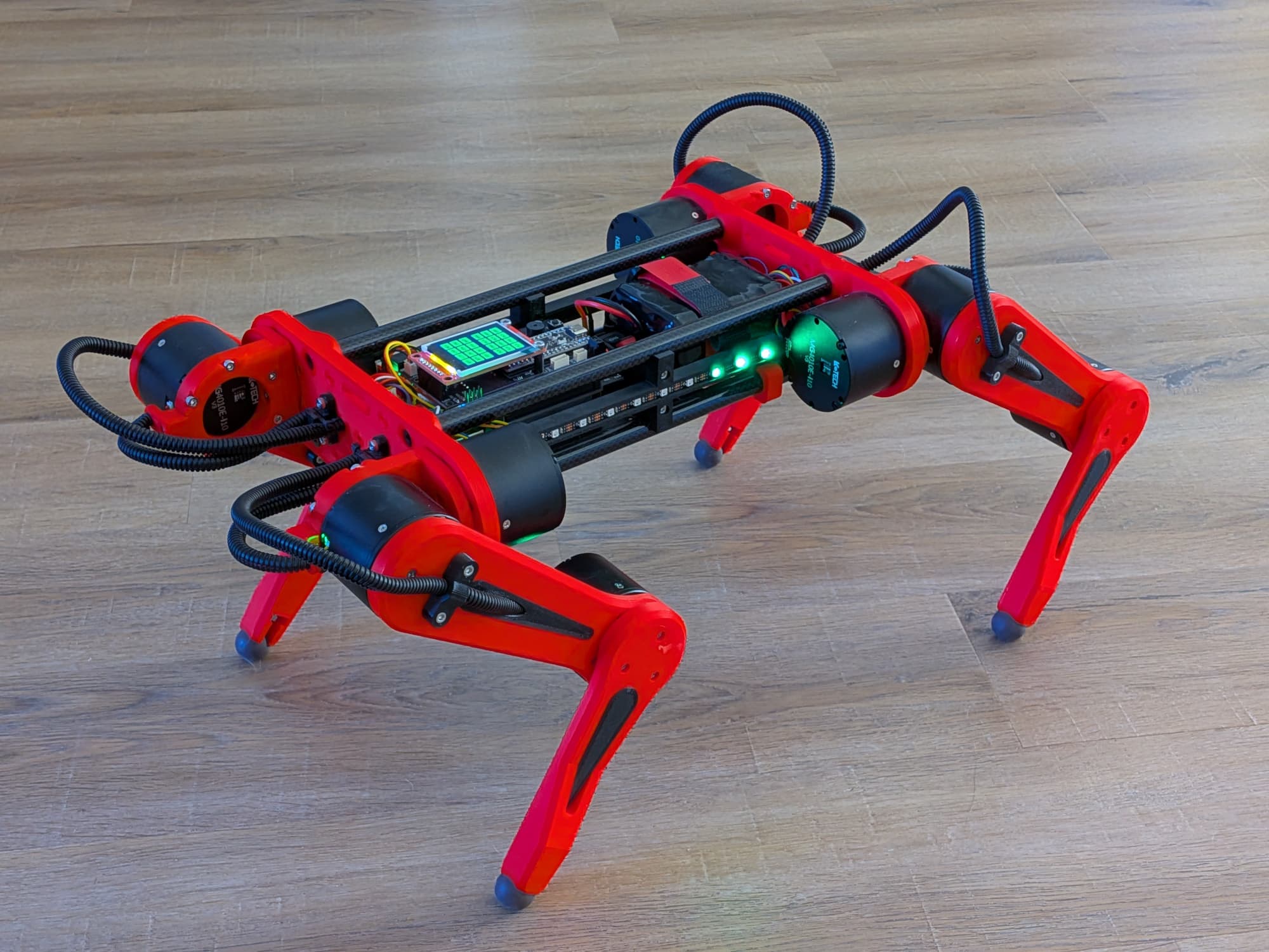 A red and black quadruped robot standing on a floor.