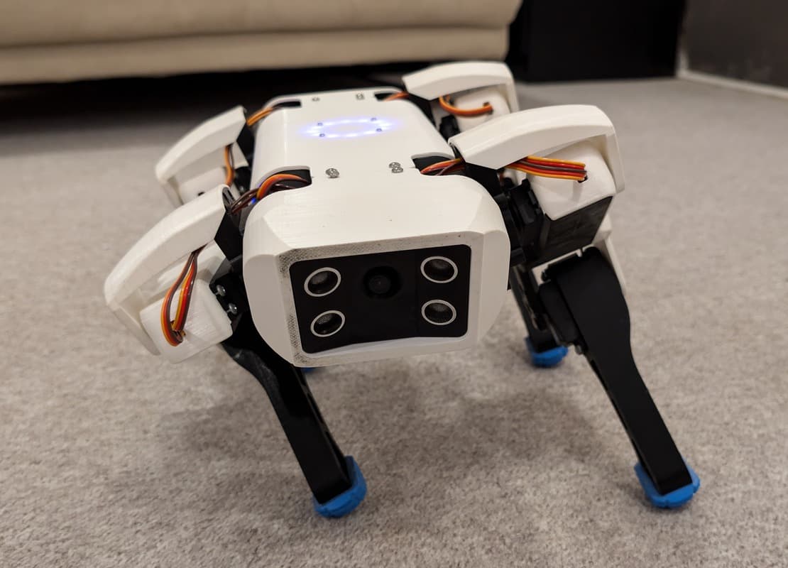 A white-bodied quadruped robot with four legs and a camera-like panel at the front.