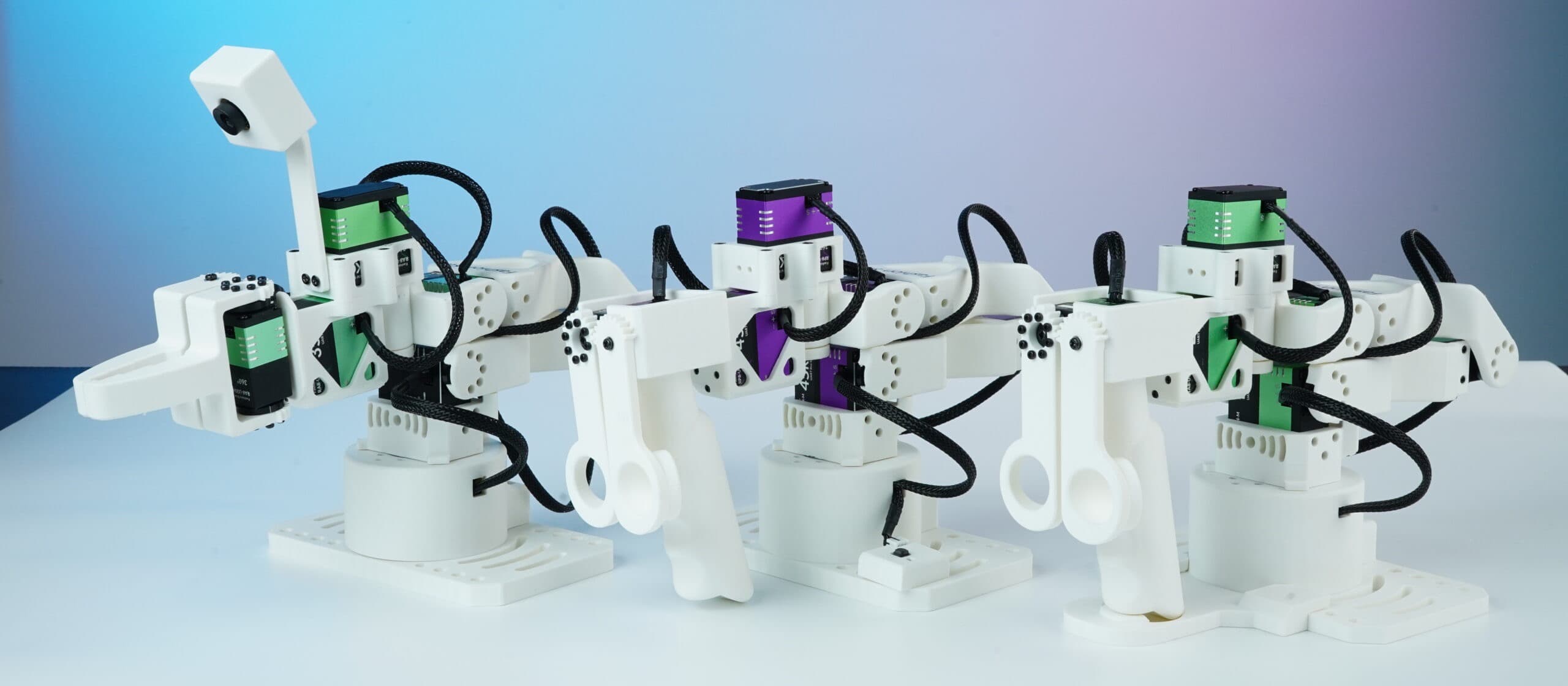Three white Star Arm 102 arms with green and purple servo modules against a blue background.
